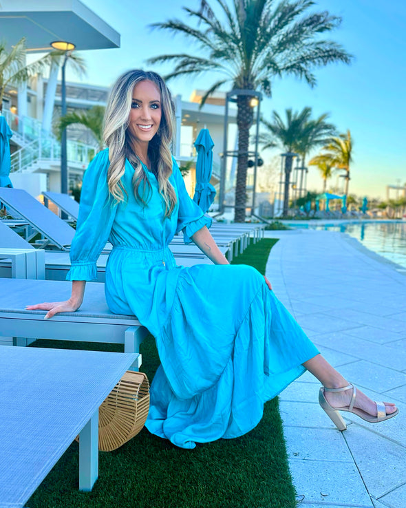 Side View of Model Seated by Pool Wearing Teal Maxi Dress with Tiered skirt and 3/4 Sleeves