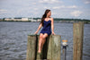 Model sitting on pier looking to the side wearing Jude Connally Bailey Dress in Navy