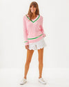Full body view of model in the Lilly Pulitzer Brockton Sweater. A light pink varsity style sweater with green accent stripes around the v neck collar, wrists, and bottom hem