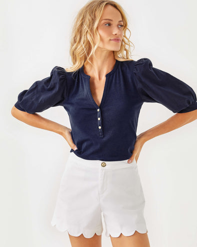 Model in the Lilly Pulitzer Buttercup Mid-Rise Short in Resort White. White scallop hem shorts with a gold button closure 