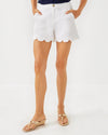 Model in the Lilly Pulitzer Buttercup Mid-Rise Short in Resort White. White scallop hem shorts with a gold button closure 