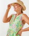 Smiling model with gold bracelets and a hat in the Lilly Pulitzer Sydnee Maxi Dress - Fauna Green - Lime Feeling Good. A sleeveless maxi dress with a notched neckline in beautiful green and pink floral pattern