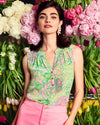 Model in the Lilly Pulitzer Sleeveless Elsa Top - Fauna Green - Lime Feeling Good paired with pink shorts, standing in front of pink and yellow flowers
