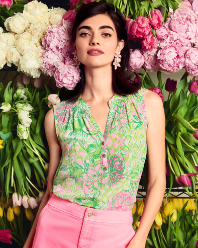 Model in the Lilly Pulitzer Sleeveless Elsa Top - Fauna Green - Lime Feeling Good paired with pink shorts, standing in front of pink and yellow flowers