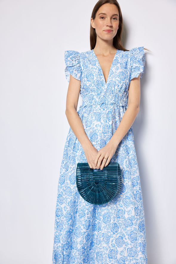 Woman wearing a blue floral dress holding a green handbag against a white background