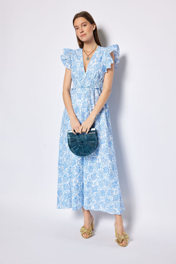 Woman wearing a blue floral dress holding a blue handbag against a white background