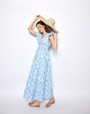 Woman wearing a blue floral dress holding a straw hat against a white background
