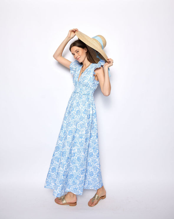 Woman wearing a blue floral dress holding a straw hat against a white background