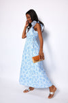 Woman wearing a light blue floral dress holding a brown clutch against a white background