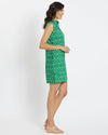 Brunette model wearing short sleeveless green and white print dress standing to the side