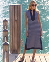 Woman in a blue and white striped midi length dress standing on a dock with water in the background