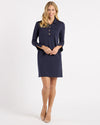 Model in the Jude Connally Midge Dress - Navy/Gold. A navy dress with gold buttons down the front, a shirt style collar, and split arm hems