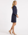Side view of model in the Jude Connally Midge Dress - Navy/Gold. A navy dress with gold buttons down the front, a shirt style collar, and split arm hems