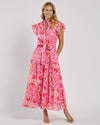 Smiling model in the Jude Connally Mirabella Dress in Gilded Garden Peony Pink Gold. A pink orange and gold midi dress with flutter sleeves and tie belt with a floral/geometric pattern