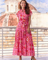 Smiling model in the Jude Connally Mirabella Dress in Gilded Garden Peony Pink Gold. A pink orange and gold midi dress with flutter sleeves and tie belt