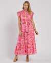Smiling model in the Jude Connally Mirabella Dress in Gilded Garden Peony Pink Gold. A pink orange and gold midi dress with flutter sleeves and tie belt with a floral/geometric pattern