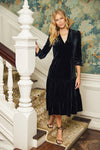 Model holding on to stair railing wearing Jude Connally Maggie Velvet Midi Dress in Black