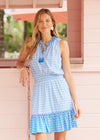 Smiling model in the Cabana Life Seaside Smocked Waist Dress. A sleeveless mini dress with a smocked waist and a tassel tie neckline 