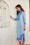 Model in a blue, long sleeved shift dress with a floral pattern and detailing at the collar, wrists, and bottom hem