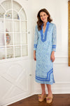 Model in a blue, long sleeved shift dress with a floral pattern and detailing at the collar, wrists, and bottom hem