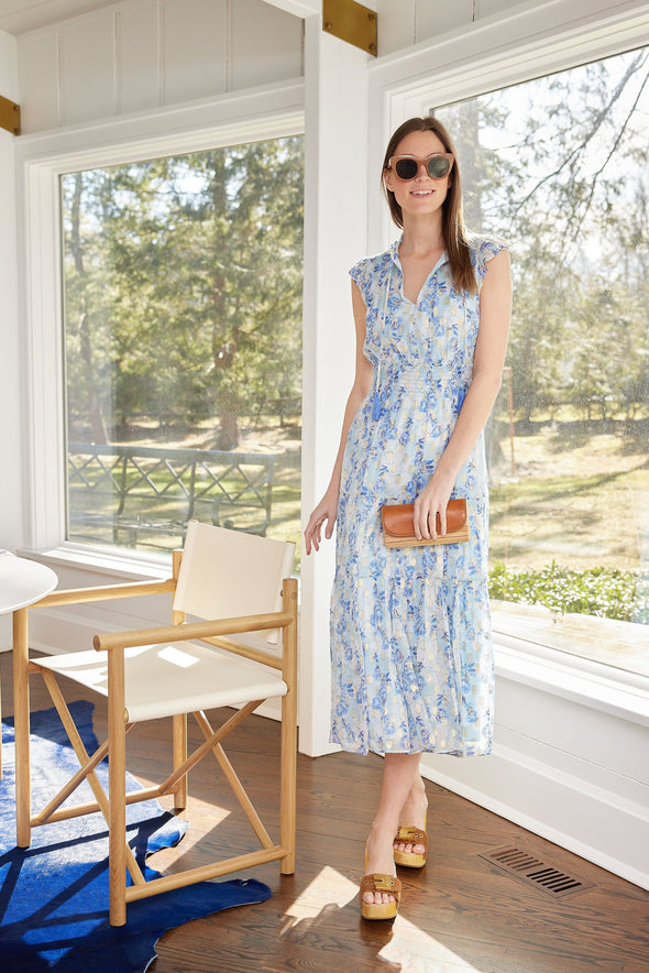 Model in a tiered midi dress with a ruched waist, flutter sleeves, and v neck. It has a beautiful blue, purple, metallic gold floral print, that is both subtle and stunning
