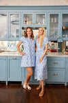 Two women in matching blue floral dresses standing in a kitchen with light blue cabinets.