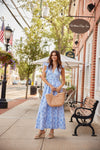 Woman in a blue dress standing on a sidewalk with a building and street in the background