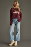 Woman wearing a maroon sweater with 'Wine Weather' text and blue jeans on a gray background
