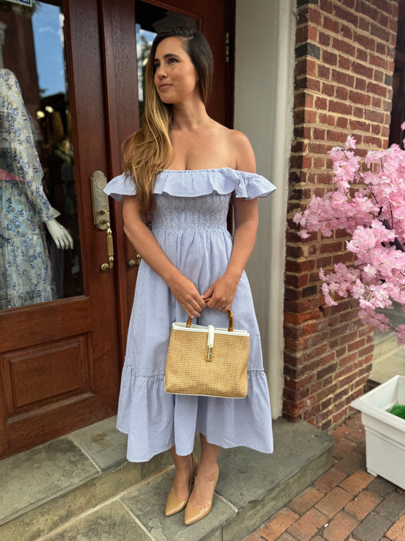 Model outside holding the Chatham Straw Bag - White. A woven bag with white trim and a bamboo handle 