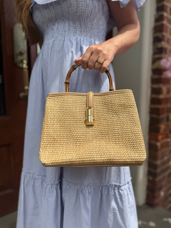 Model outside holding the Chatham Straw Bag - tan. A woven bag with tan trim and a bamboo handle 