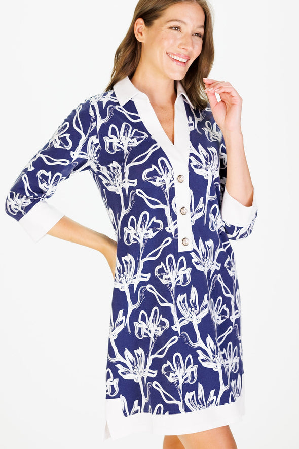 Smiling model in the Duffield Lane June Dress - Navy Painted Flower. It has 3/4 sleeves and white trim around collar, cuffs, and hem, with white flowers on a navy background