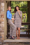 Blonde woman wearing blue top and brown plaid pants leans against doorframe next to a brunette woman in a 3/4 sleeve dress in the same brown plaid print