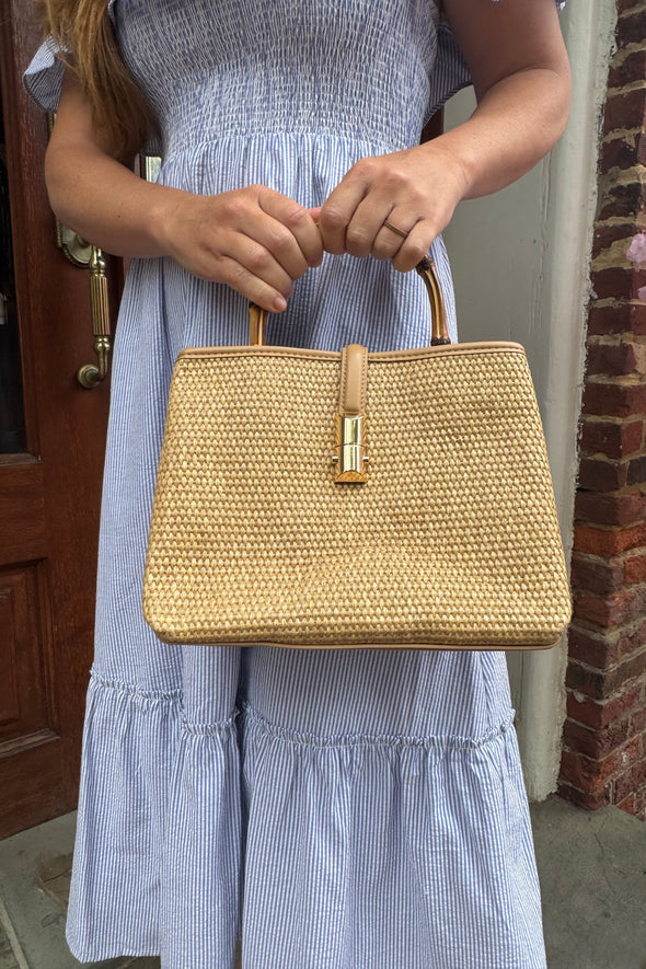 Model outside holding the Chatham Straw Bag - tan. A woven bag with tan trim and a bamboo handle 
