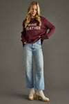 Woman wearing a maroon sweater with 'WINE WEATHER' text, blue jeans, and white boots on a gray background