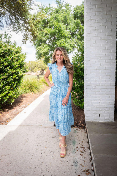 Model wearing a tiered maxi dress in a blue floral print with a ruched waist and flutter sleeves.