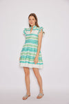Model in a short flowy dress with flutter sleeves and a v-neck, with green and aqua prints in a stripe pattern. 