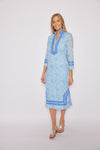 Model in a blue, long sleeved shift dress with a floral pattern and detailing at the collar, wrists, and bottom hem
