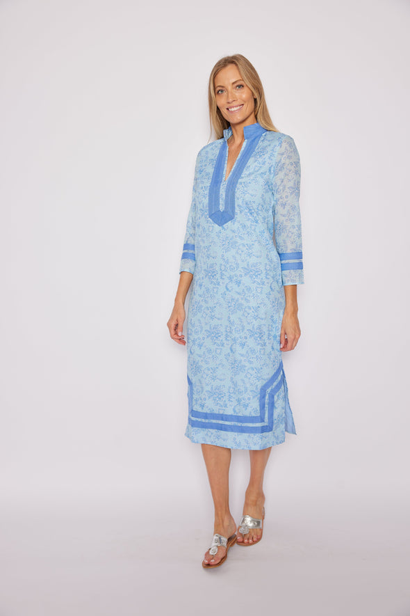 Model in a blue, long sleeved shift dress with a floral pattern and detailing at the collar, wrists, and bottom hem