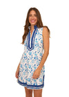 Smiling model in the Cabana Life Bubbly Sleeveless Tunic Cover Up. A sleeveless mock neck shift dress with blue flowers on a white background and royal blue trim around the neckline and bottom hem