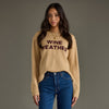 Woman wearing a beige sweater with 'WINE WEATHER' text against a gray background