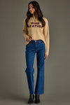 Woman wearing a beige sweater with 'WINE WEATHER' text and blue jeans on a gray background