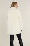 Back view of model in the Dolce Cabo Faux Fur Coat - Ivory, a faux fur mid-thigh coat, featuring a fold over collar and pockets