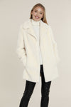 Smiling model in the Dolce Cabo Faux Fur Coat - Ivory, a faux fur mid-thigh coat, featuring a fold over collar and pockets