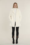 Smiling model in the Dolce Cabo Faux Fur Coat - Ivory, a faux fur mid-thigh coat, featuring a fold over collar and pockets
