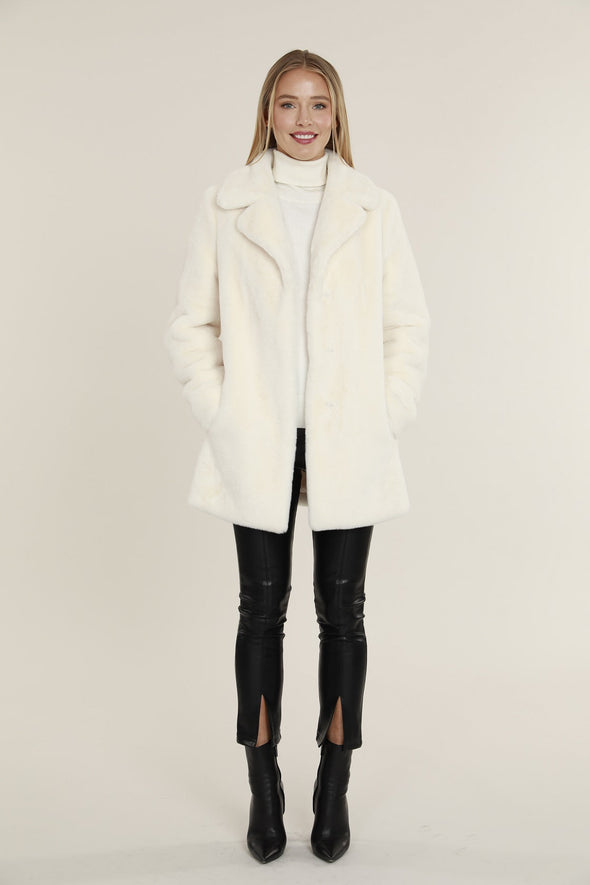 Smiling model in the Dolce Cabo Faux Fur Coat - Ivory, a faux fur mid-thigh coat, featuring a fold over collar and pockets