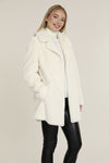 Smiling model in the Dolce Cabo Faux Fur Coat - Ivory, a faux fur mid-thigh coat, featuring a fold over collar and pockets