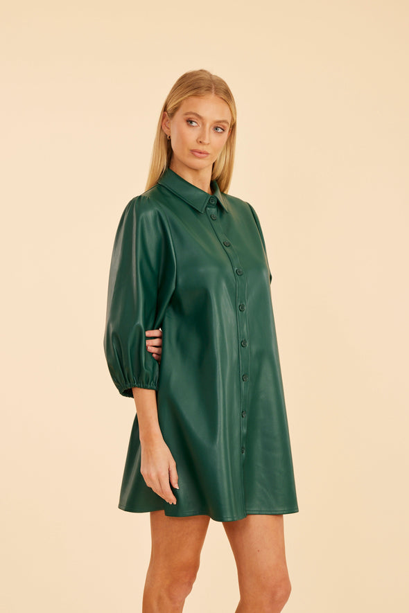 Model is wearing the Dolce Cabo Soft Vegan Leather Dress in Forest Green. A mini shift silhouette with soft faux leather, 3/4 puff sleeves, and front button detailing