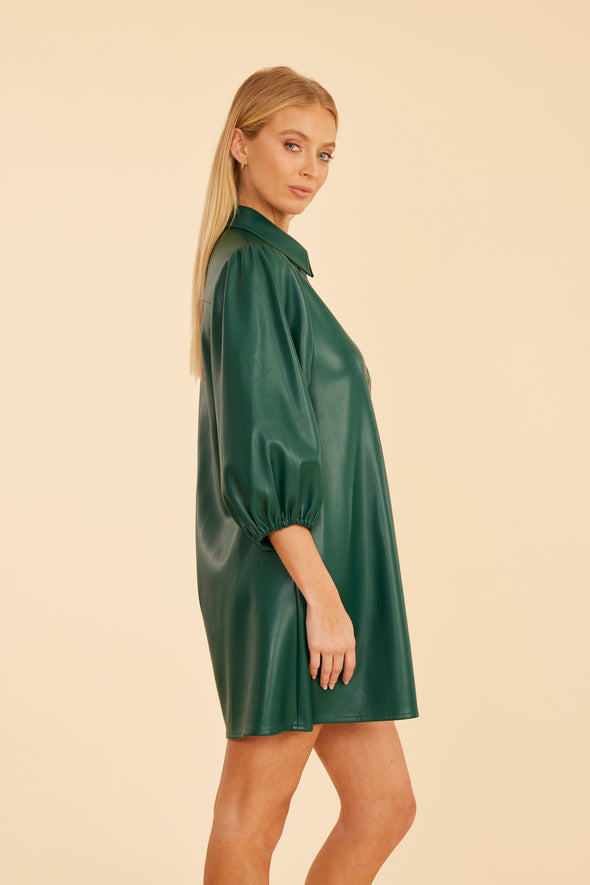Side view of model wearing the Dolce Cabo Soft Vegan Leather Dress in Forest Green. A mini shift silhouette with soft faux leather, 3/4 puff sleeves, and front button detailing