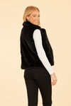 Model looking over her shoulder in the Dolce Cabo Faux Fur Vest in Black, featuring a cozy fold-over collar and pockets