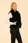 Side view of model wearing the Dolce Cabo Faux Fur Vest in Black, featuring a cozy fold-over collar and pockets. 